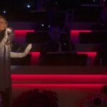 Mariah Carey de cuerpo completo cantando en un show navideno, con vestido gris y guantes largos
