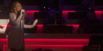 Mariah Carey de cuerpo completo cantando en un show navideno, con vestido gris y guantes largos