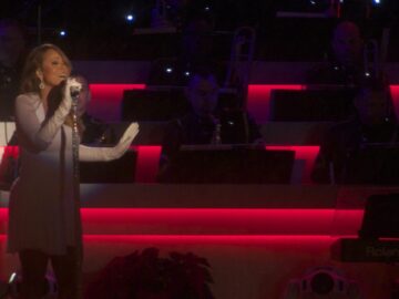Mariah Carey de cuerpo completo cantando en un show navideno, con vestido gris y guantes largos