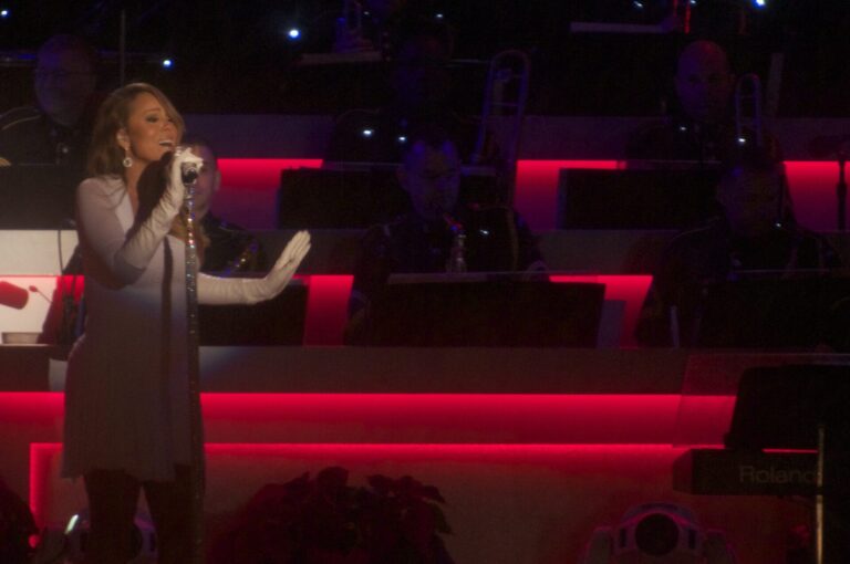 Mariah Carey de cuerpo completo cantando en un show navideno, con vestido gris y guantes largos