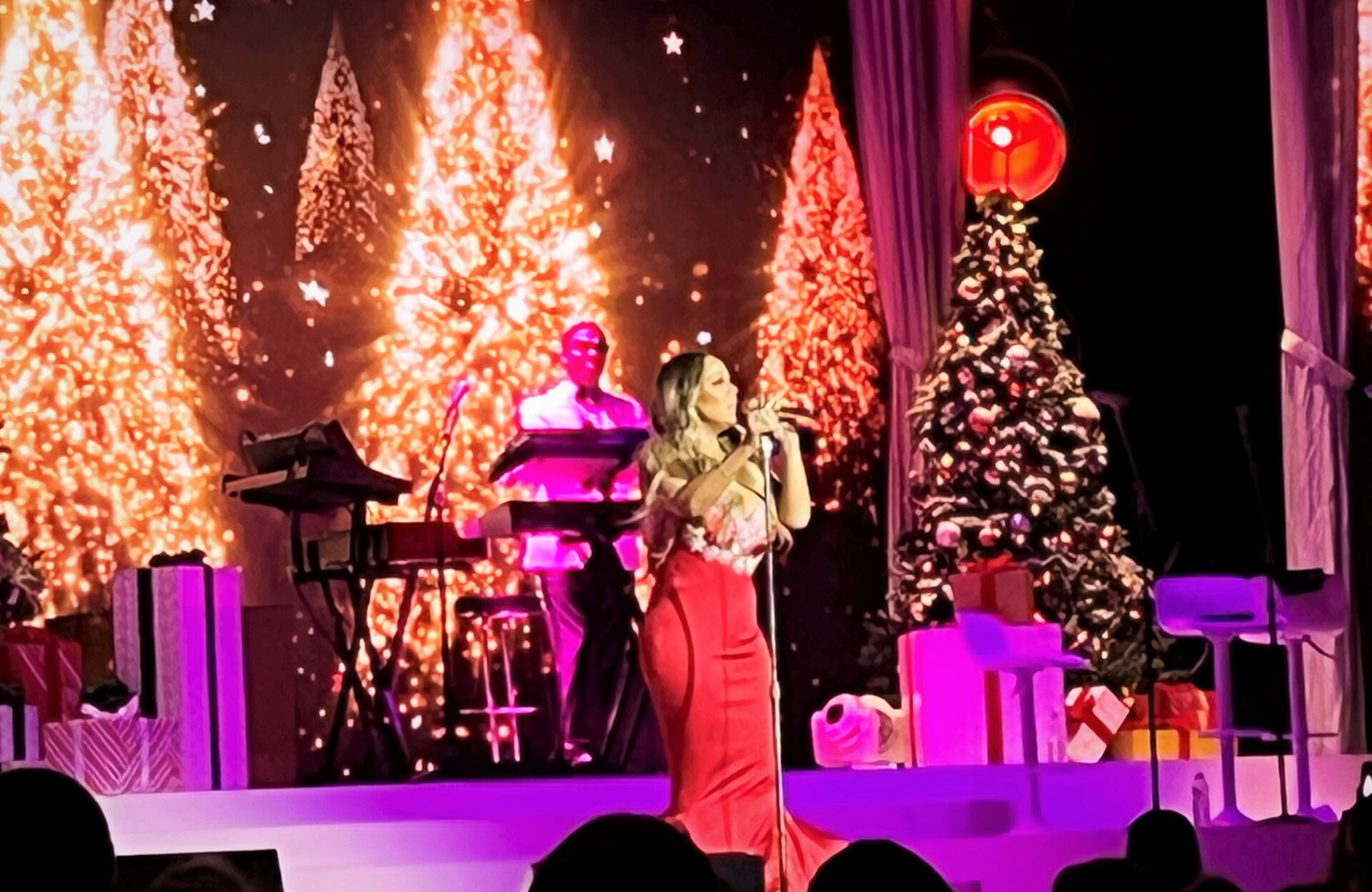 Mariah Carey cantando en un escenario decorado con árboles de Navidad y regalos durante una presentación en Toronto